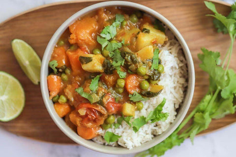 easy thai red pumpkin and vegetable curry pot served with rice, coriander and fresh lime in a while bowl 