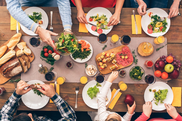 image looking down onto a table of healthy meals and colourful fruit and vegetables and salad with hands reaching in to help themselves to it