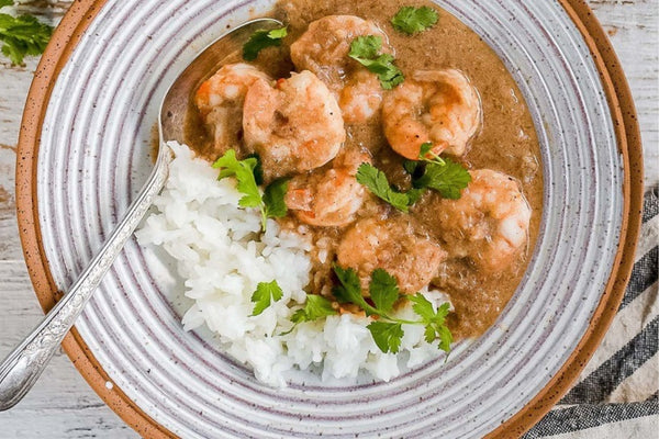 Malai king prawn curry with jasmine rice served with fresh coriander on the top in a ceramic bowl with white glaze and brown edging