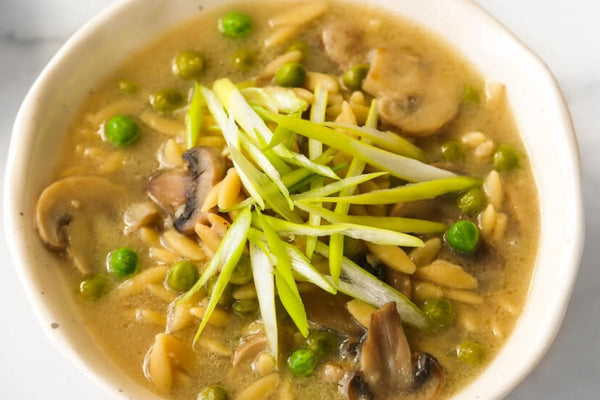 image from above looking down on a large white ceramic bowl filled with appetising mushroom and orzo pasta soup topped with a garnish of thinly sliced spring onions