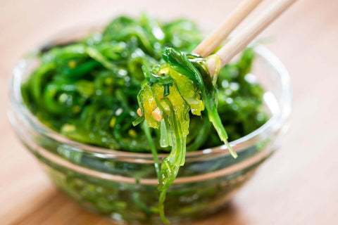 A glass bowl of fresh green sea weed or sea kelp ready to eat and chop sticks on the side