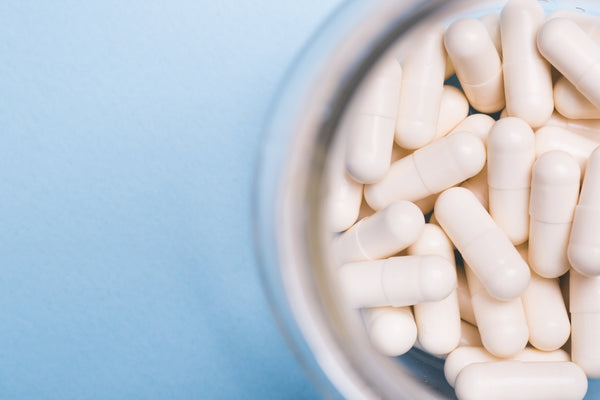 Image viewed from above of a small round white ceramic bowl filled with light coloured selenium capsules on a blue background