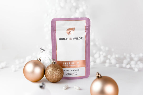 Lifestyle image of Birch & Wilde Selenium Capsules refill pouch against a white background with gold and white Christmas bauble decorations scattered around it