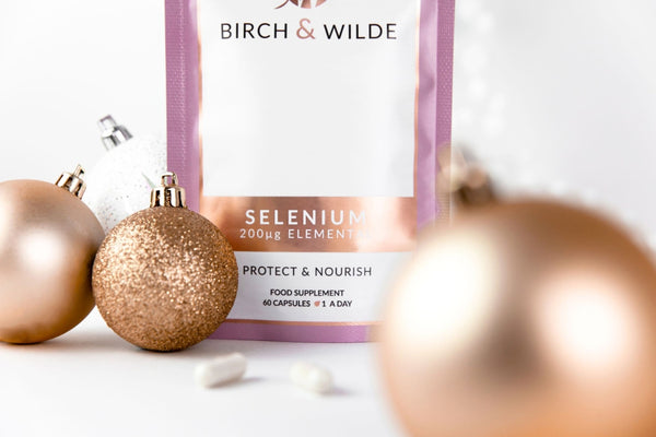 Close up image of Birch & Wilde Selenium Capsules refill pouch against a white background with gold and white Christmas bauble decorations scattered around it