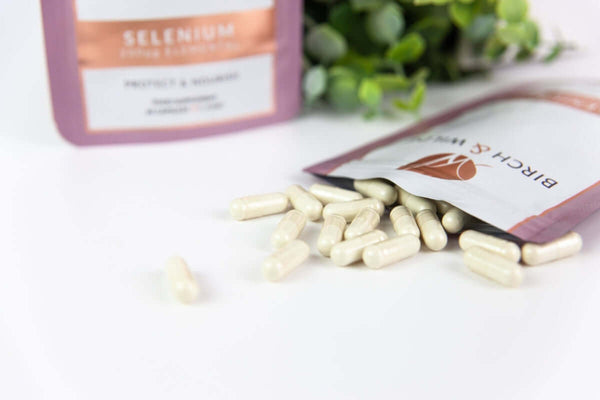 Selenium capsules health supplement refill pouch from Birch & Wilde with Selenium capsules spilling out and a green plant in the background