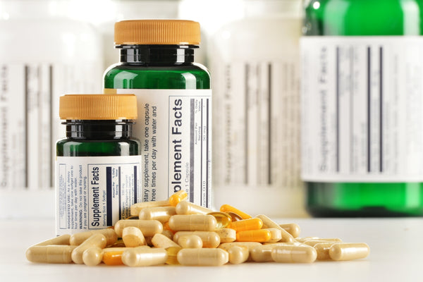 horizontal view on a small pile of supplements capsules and tablets with empty green supplement bottles in the background with labels saying supplement facts on them