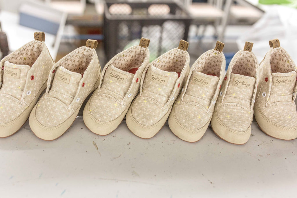 Nahaufnahme von sieben gleich großen Wildling Shoes Minimalschuhen in Kleinkindgröße, die aufgereiht nebeneinander stehen.