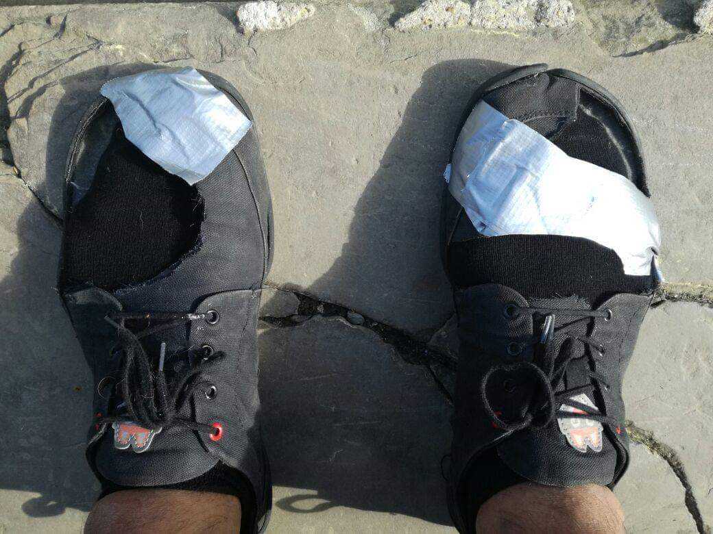 Close-up of two feet standing on a rock slab in black Wildling Shoes. The shoes are cut up in the front and taped, as prototypes of a minimal shoe sandal.