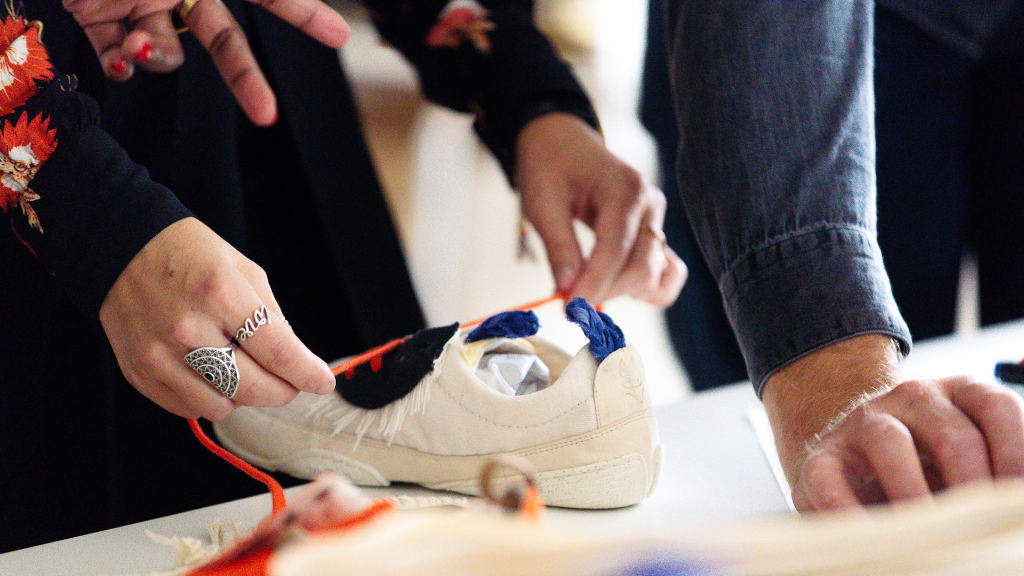 Close-up of a Wildling shoe prototype on a desk. The hands of different people are holding the shoe or pointing to it.
