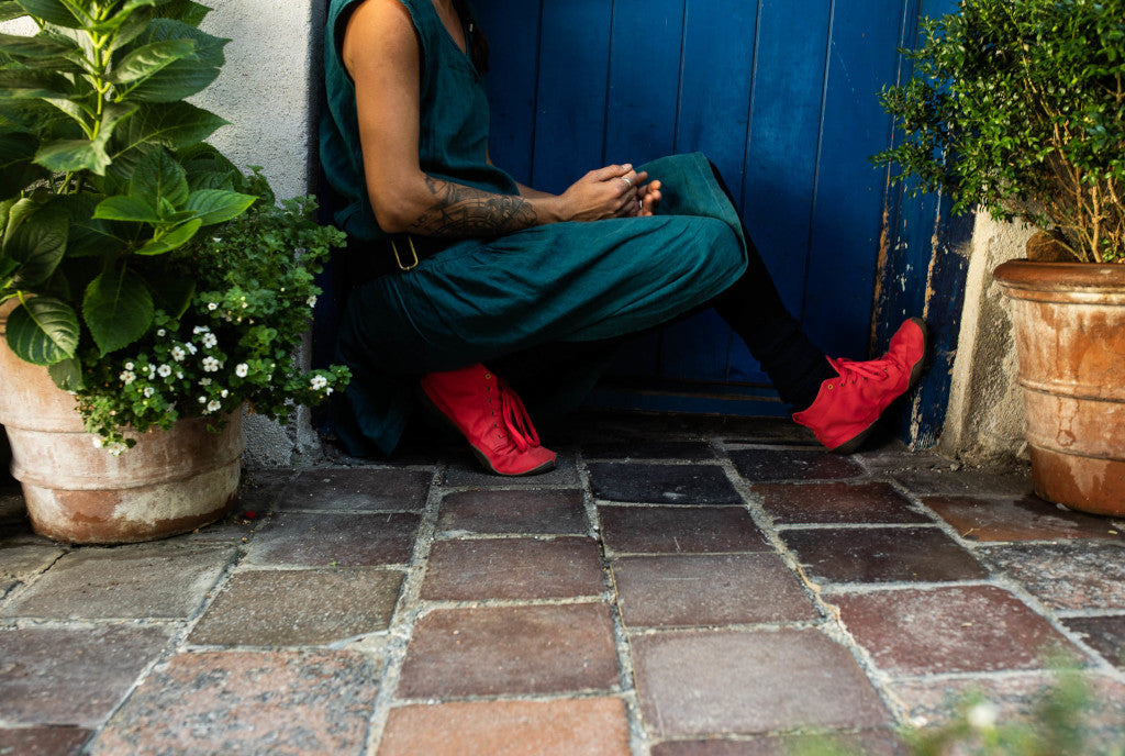 A person in a squatting position, up to their shoulders in the picture, wearing bright red Wildling barefoot shoes on their feet.