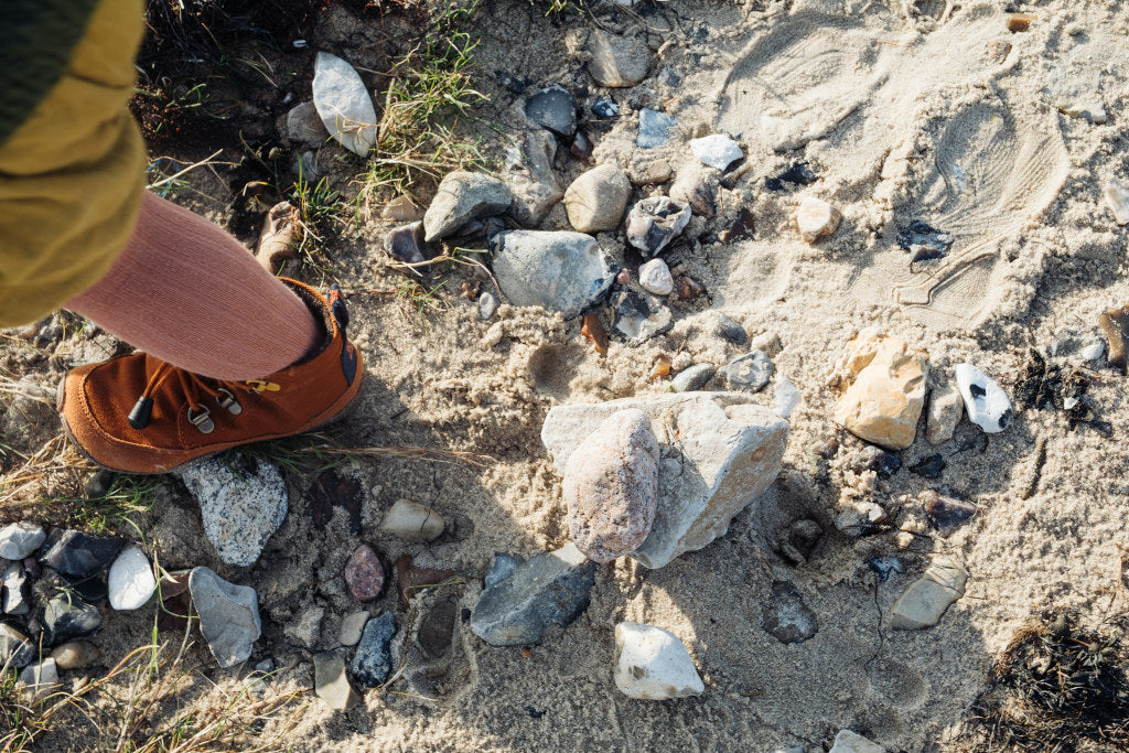 Nahaufnahme: ein Kinderfuß in einem Wildling Barfußschuh auf einem sandig-steinigen Untergrund.