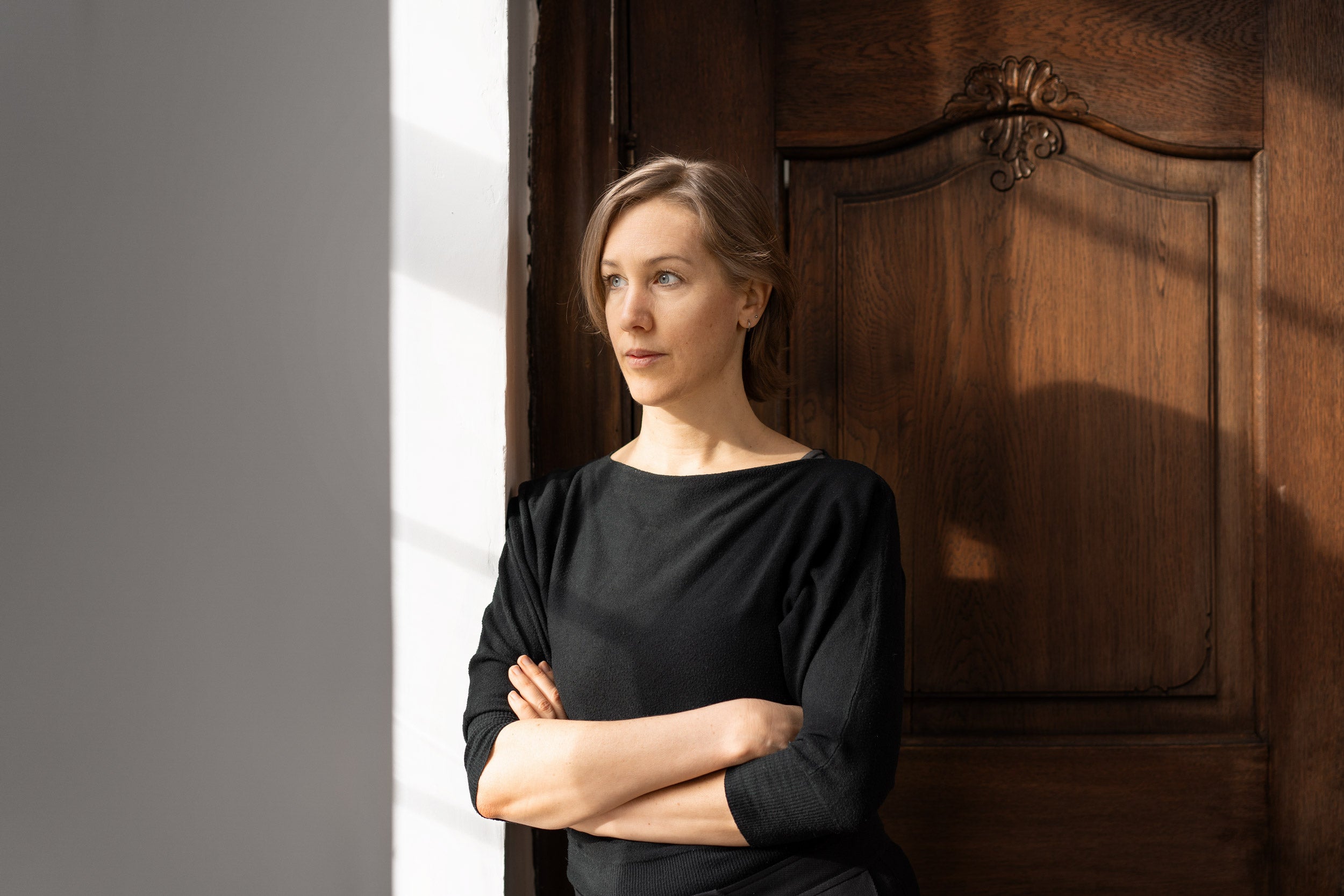 Wildling founder Anna Yona stands in an interior against a white and brown background, looking out the window.