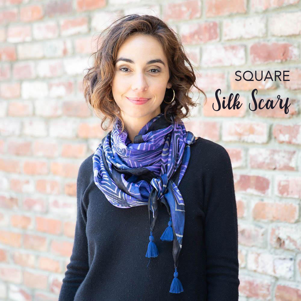 woman wearing a purple and blue printed silk square scarf in front of a brick wall
