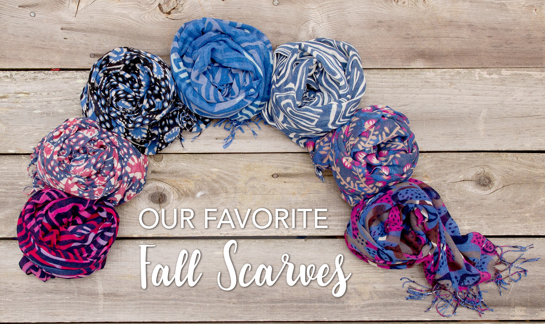 Flat lay on wood panels of coiled, colorful, fall scarves in blues and berries