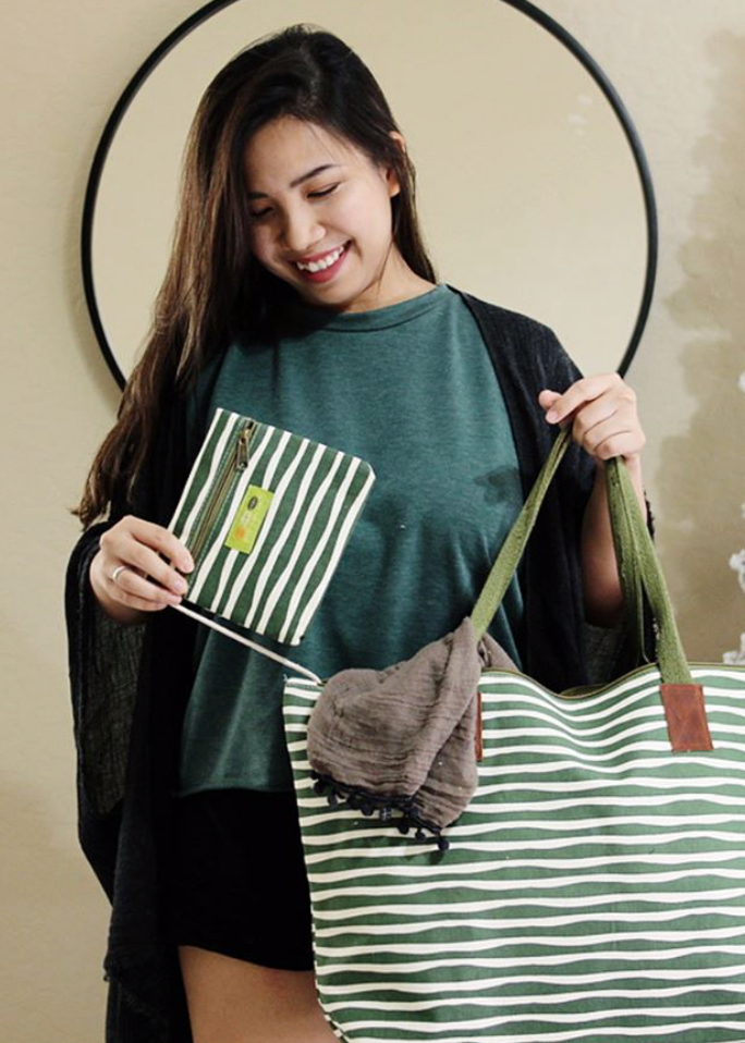 woman wearing green tshirt with black fringe kimono holding a green and white striped tote bag