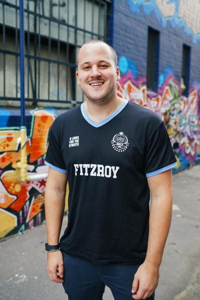 Nick Pearce standing in a Melbourne laneway, wearing black t shirt with the word "Fitzroy" on the front.