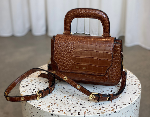  A closeup image of a brown Sans Beast vegan handbag on a cream terrazzo plinth