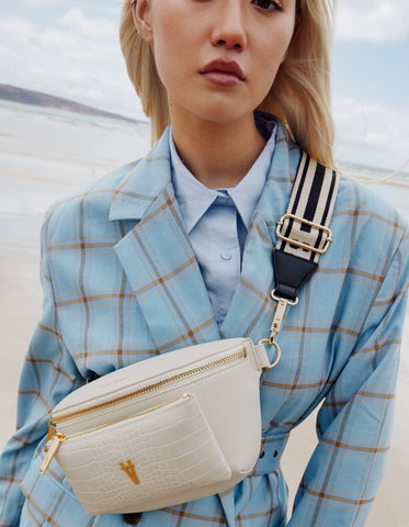 Closeup image of Dechen wearing a blue checked suit with a cream crossbody bag + striped webbing strap.