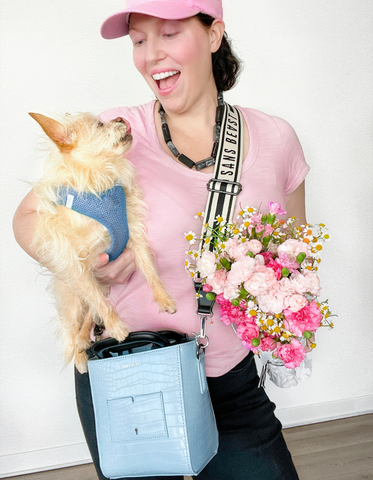 Rachel Steenland wears a pink t shirt + hat with a light blue Sans Beast vegan bag.  She is holding her dog under one arm.