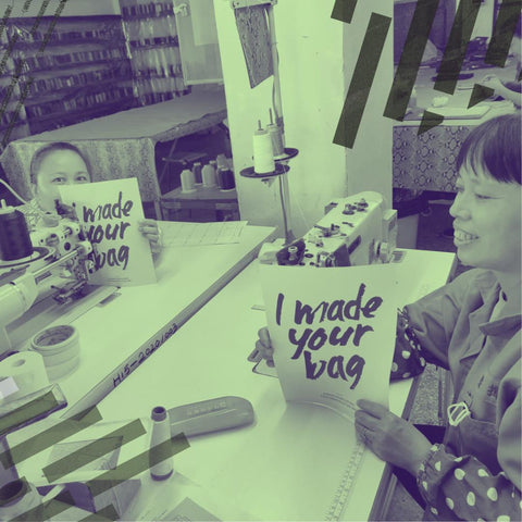 Two women sit opposite each other smiling and holding signs reading 'I made your bag.'