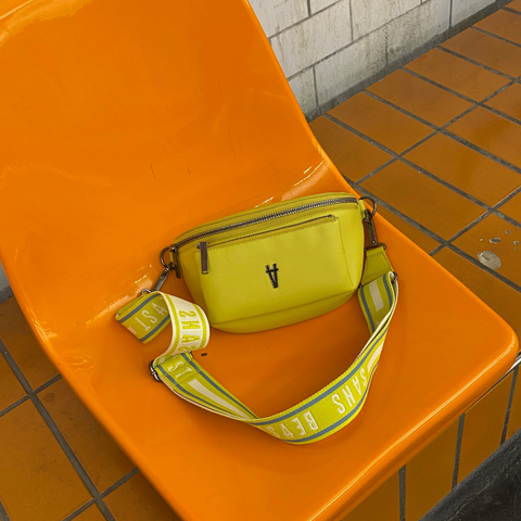 Image of a yellow Sans Beast bag + strap sitting on an orange chair at a Milan train station