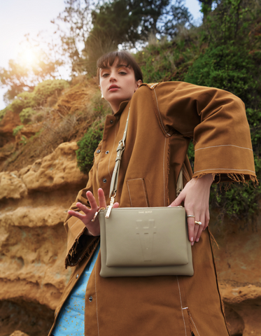 Paris wears a tan toned coat and holds a sandy coloured Sans Beast vegan handbag in front of her.