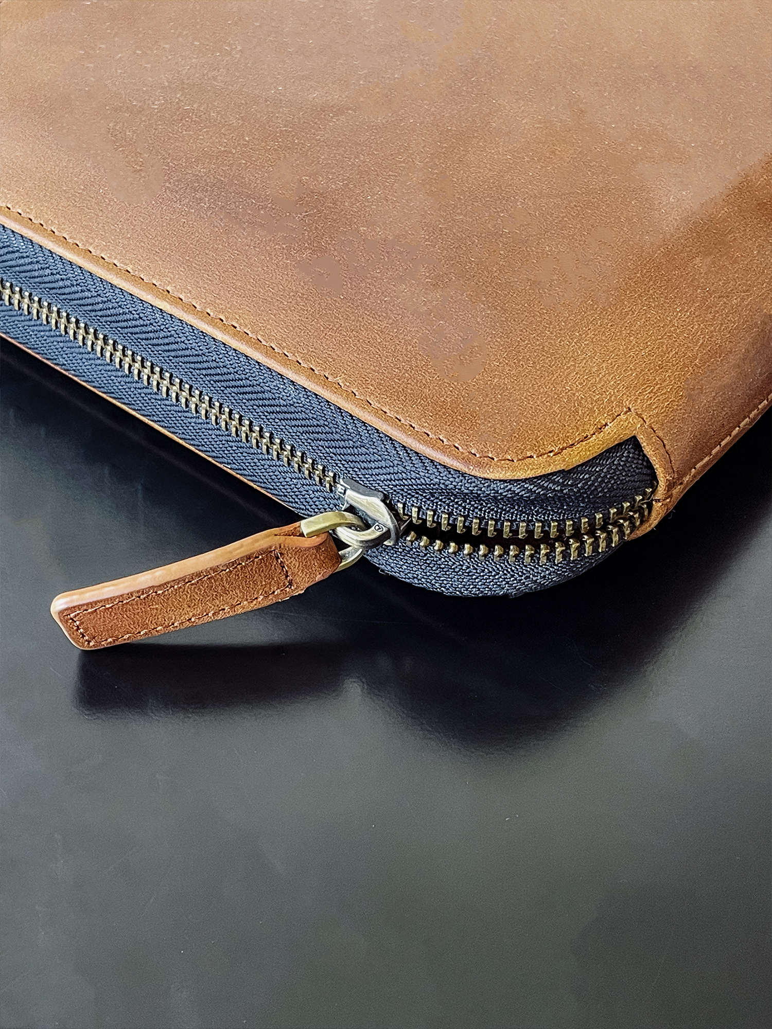 Close-up of a brown leather bag with a zipper on a dark surface.