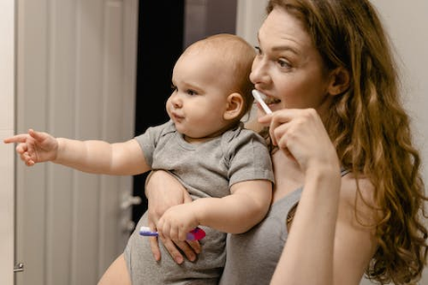  A person brushing their teeth while holding the cutest chubby-cheeked baby in the world.