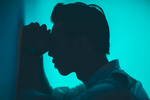 A man standing with his head and hands placed against a wall.