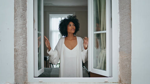 woman with natural hair looking out the window in a white nightgown