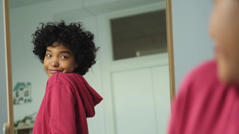 woman with natural hair smiling with confidence in the mirror
