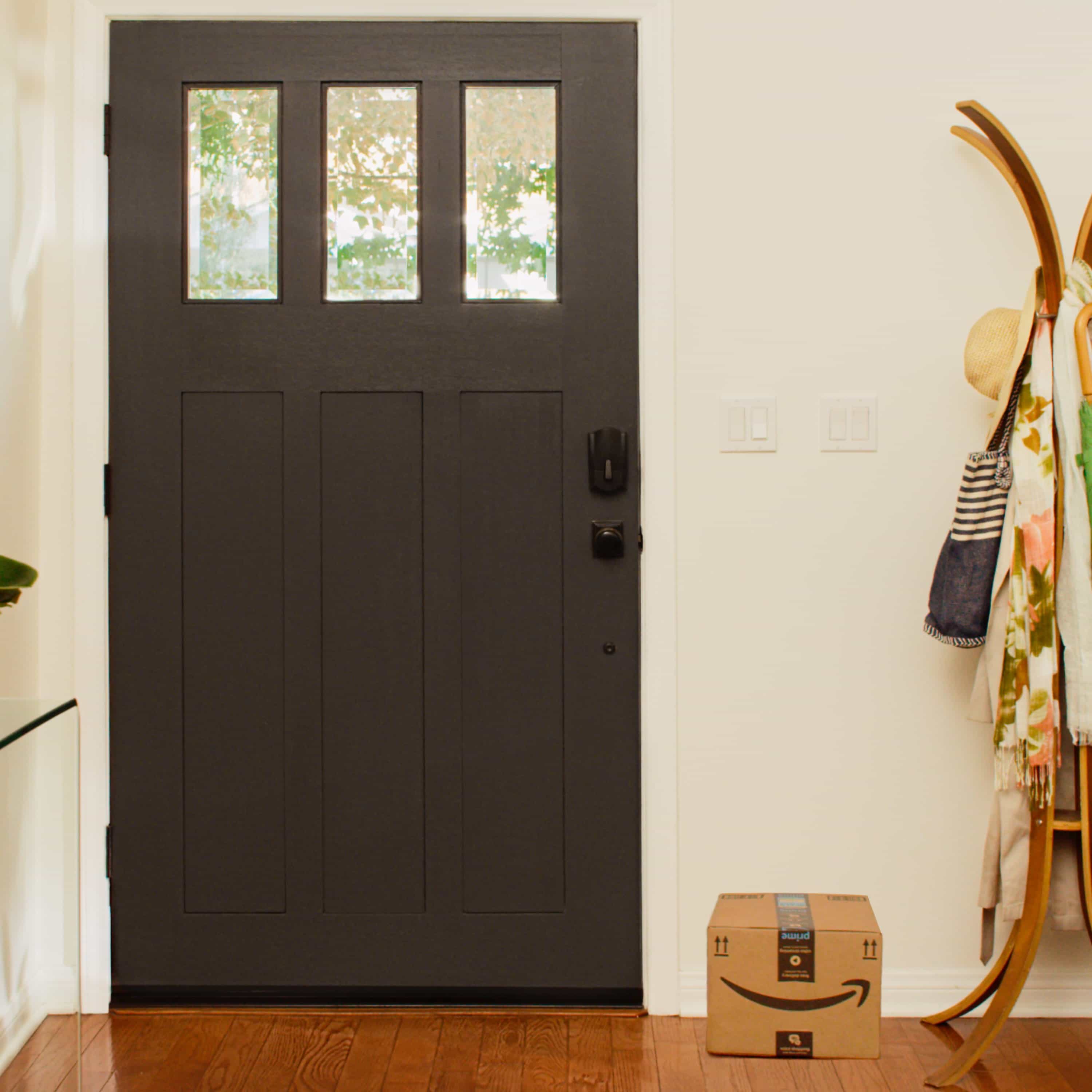 Schlage Encode Smart WiFi Deadbolt with Camelot Trim (for Works with Ring Video Doorbells and Cameras) - In the entryway of a home, a front door is equipped with a Schlage Encode Smart WiFi Deadbolt with Camelot Trim. An Amazon package is on the floor.