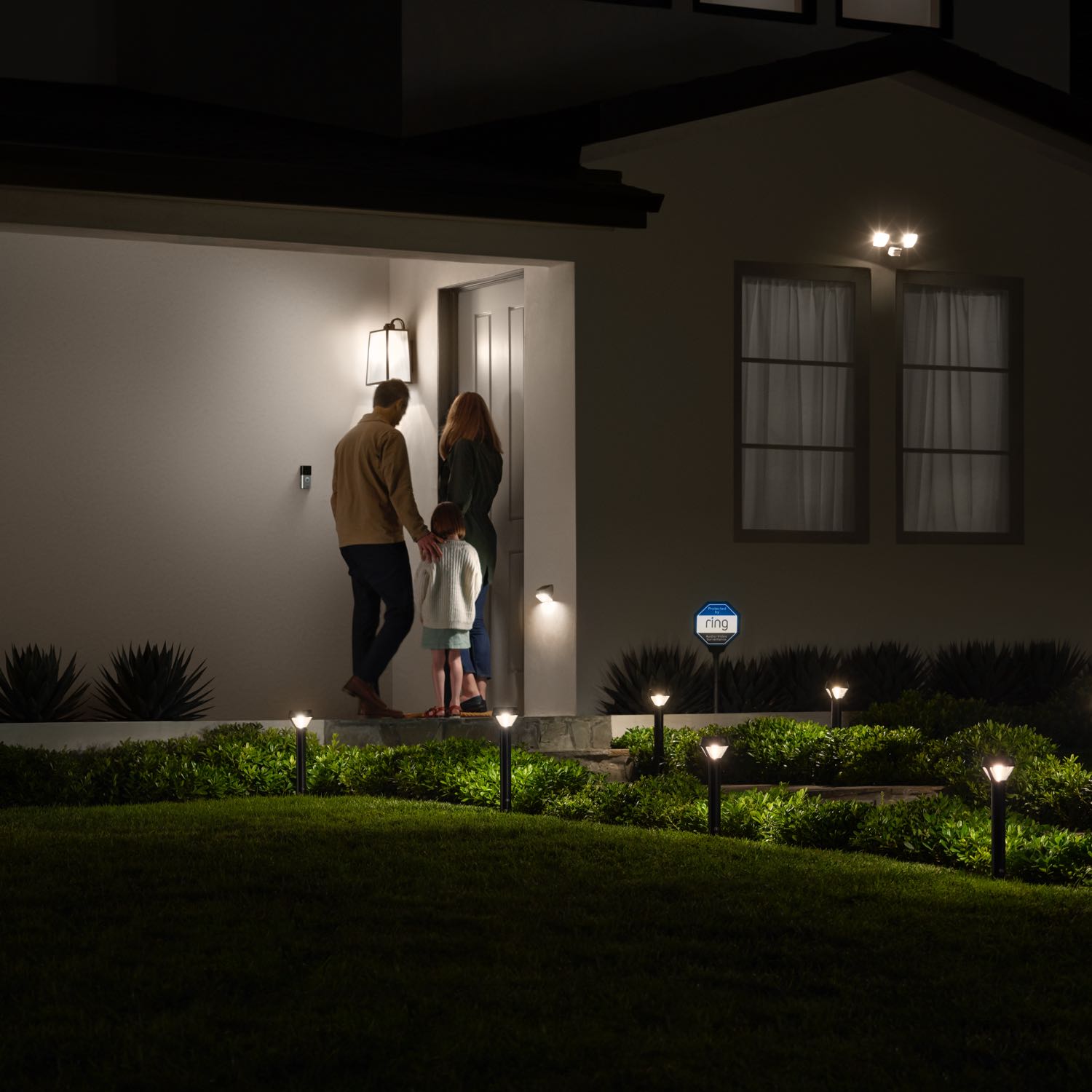 Smart Lighting Pathlight Battery - Outdoors at night, a family approaches the front door of a home. The pathway is illuminated by Solar Pathlights.