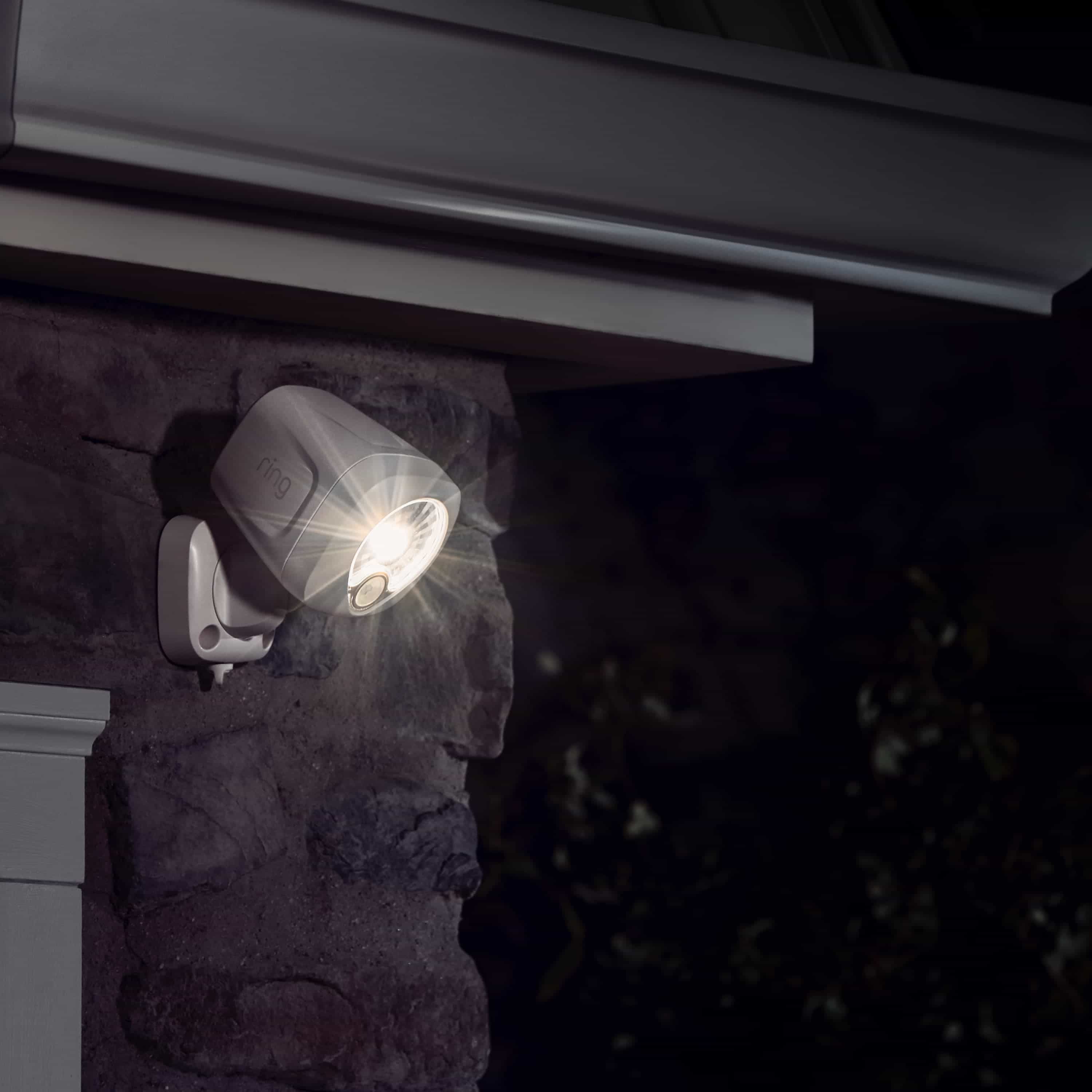 Smart Lighting Spotlight Battery - Outside at night, an illuminated Spotlight Battery is mounted to a rock wall near the corner of a home.