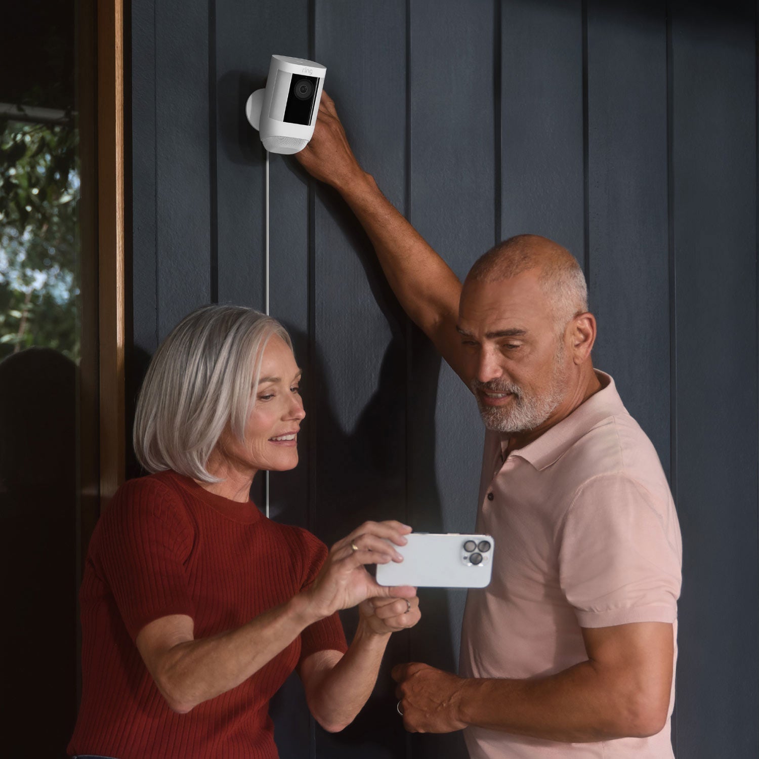 Spotlight Cam Pro (Plug-In) - Woman and man looking at smartphone while installing Spotlight Cam Pro Plug-In model on exterior wall of home.