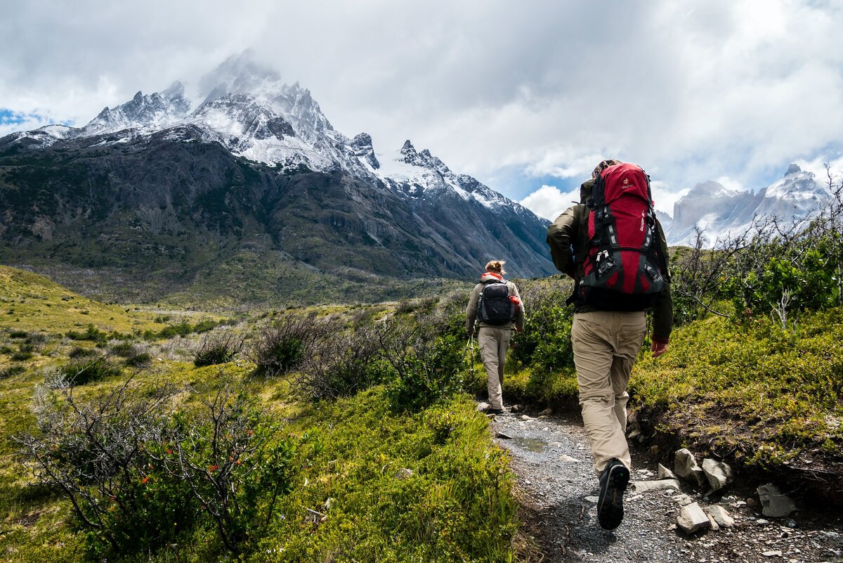 Two people with backpacks walking up to a mountain range