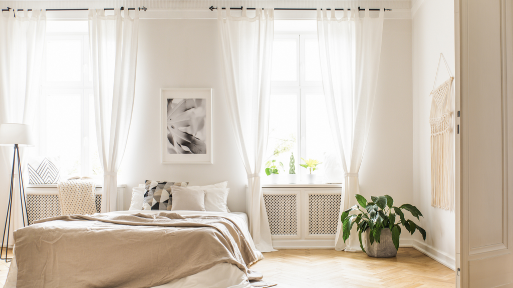 Dormitorio blanco con cortinas blancas y almohadas blancas.
