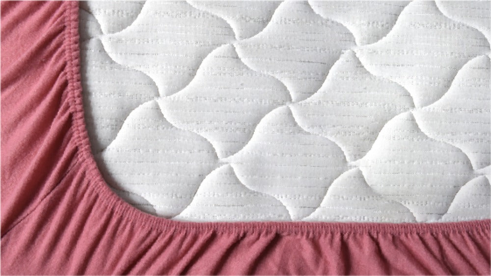 cojines mashini de color rosado y beige en una cama con un cubrecama mashini rosado