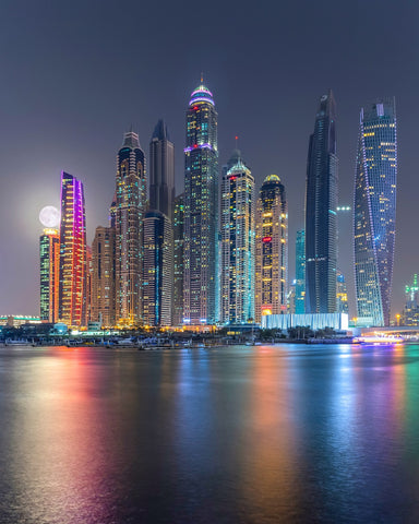 Colorful Dubai city at night with the moon in the back