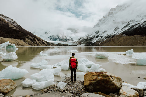 Man in red jacket standing on snow covered ground near lake