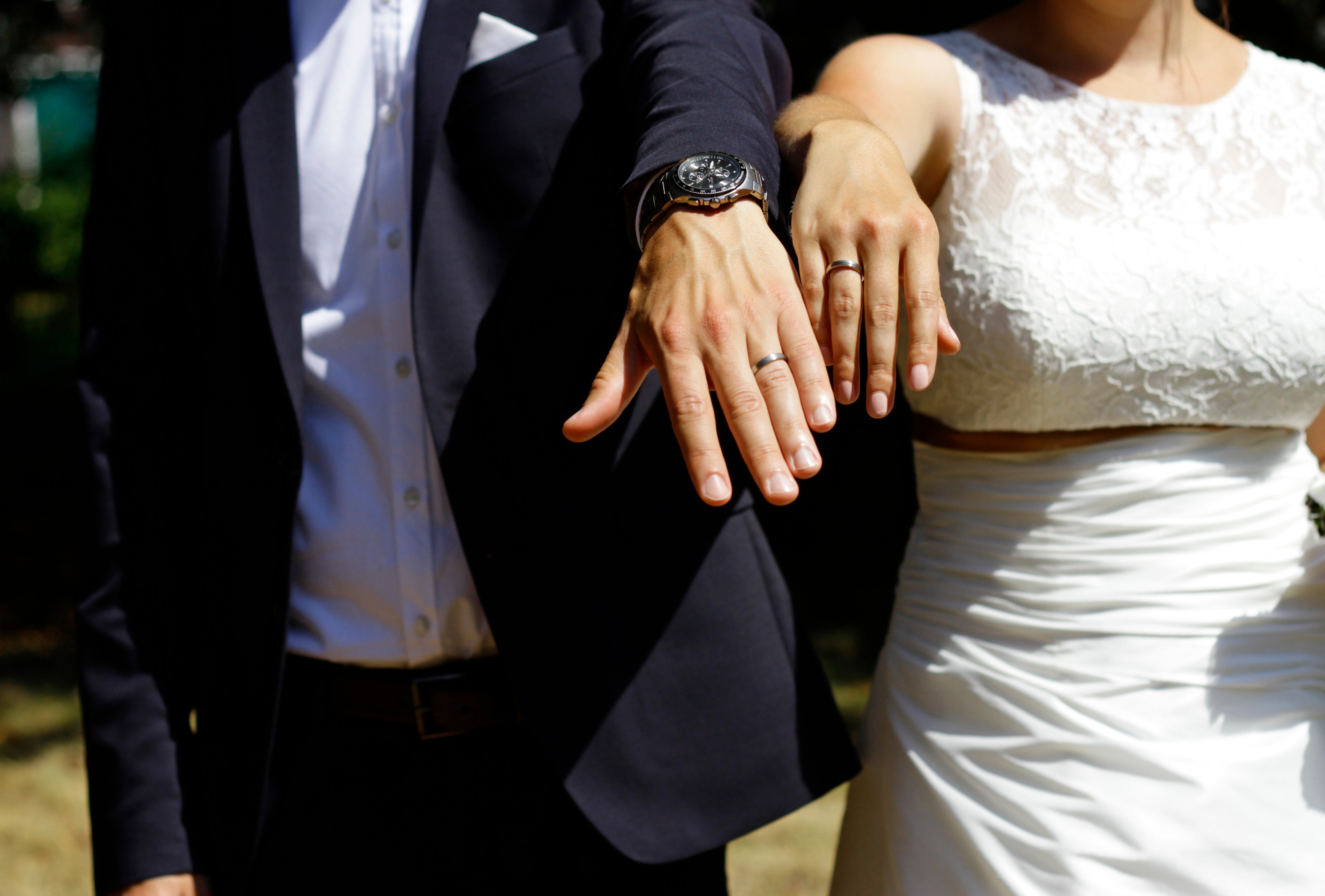 man in black suit and woman in white wedding dress showing their wedding rings