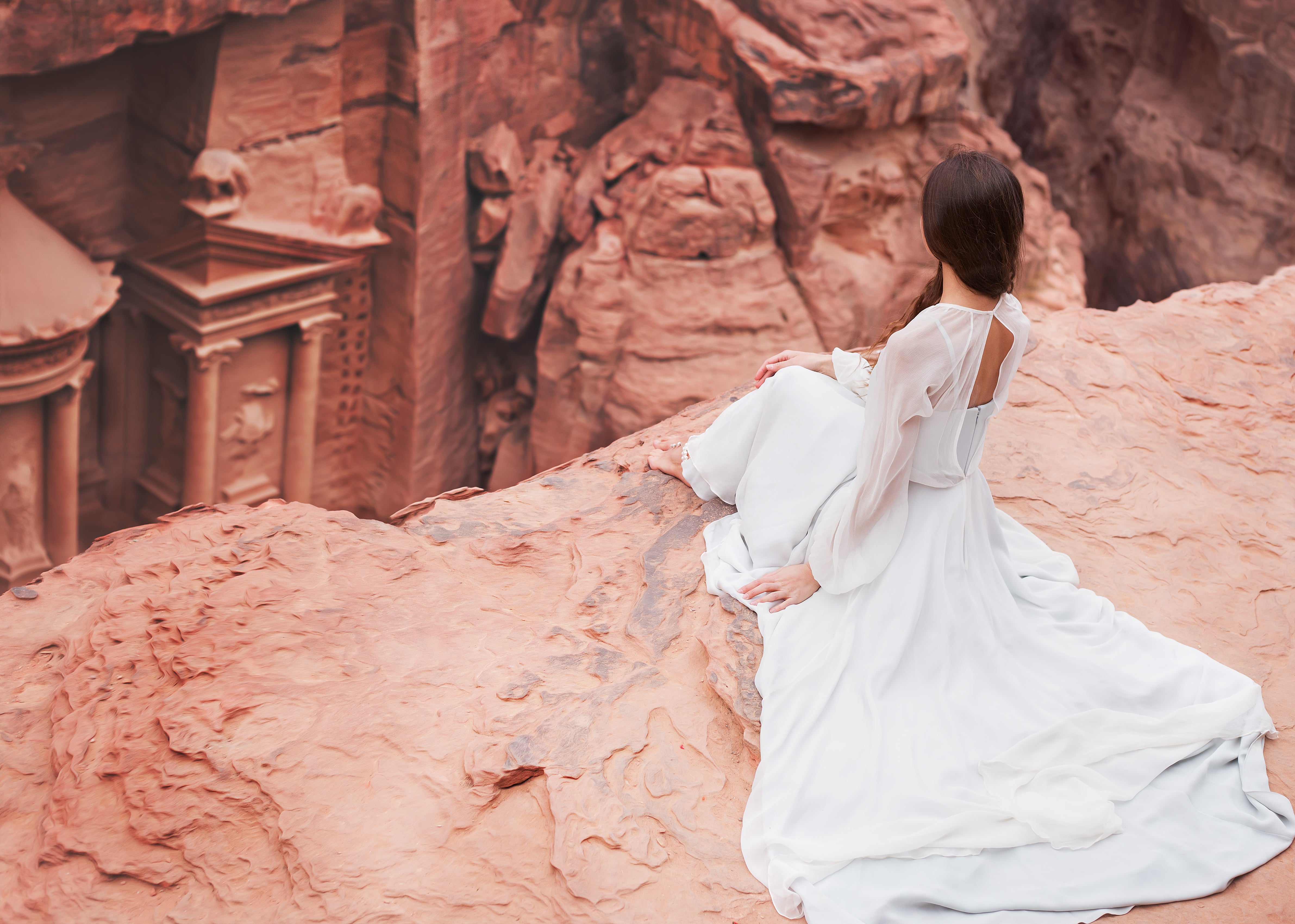 woman in white dress sitting next to a big brown rock