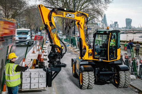 Wheeled excavator being used with excavator pallet forks to move material along a roadside