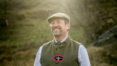 Man standing in a field wearing Schoffel Tweed Waistcoat and tweed cap