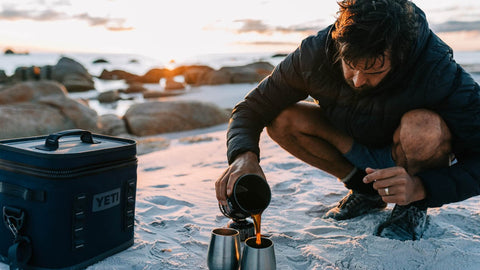 Man pouring coffee from a yeti cup on the beach