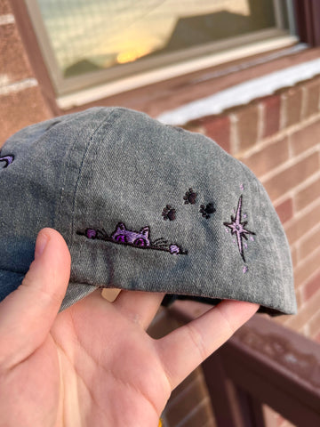 An updated embroidery sample of Faithful peeking up at you with three paw prints on a hat.