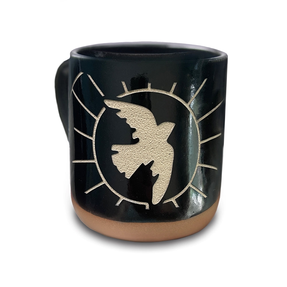 A black slip ceramic mug carved with an image of a soaring dove in front of the sun