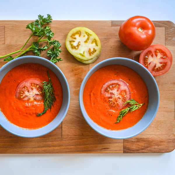 two bowls of roasted red pepper and tomato soup garnished with fresh dill and fresh tomato
