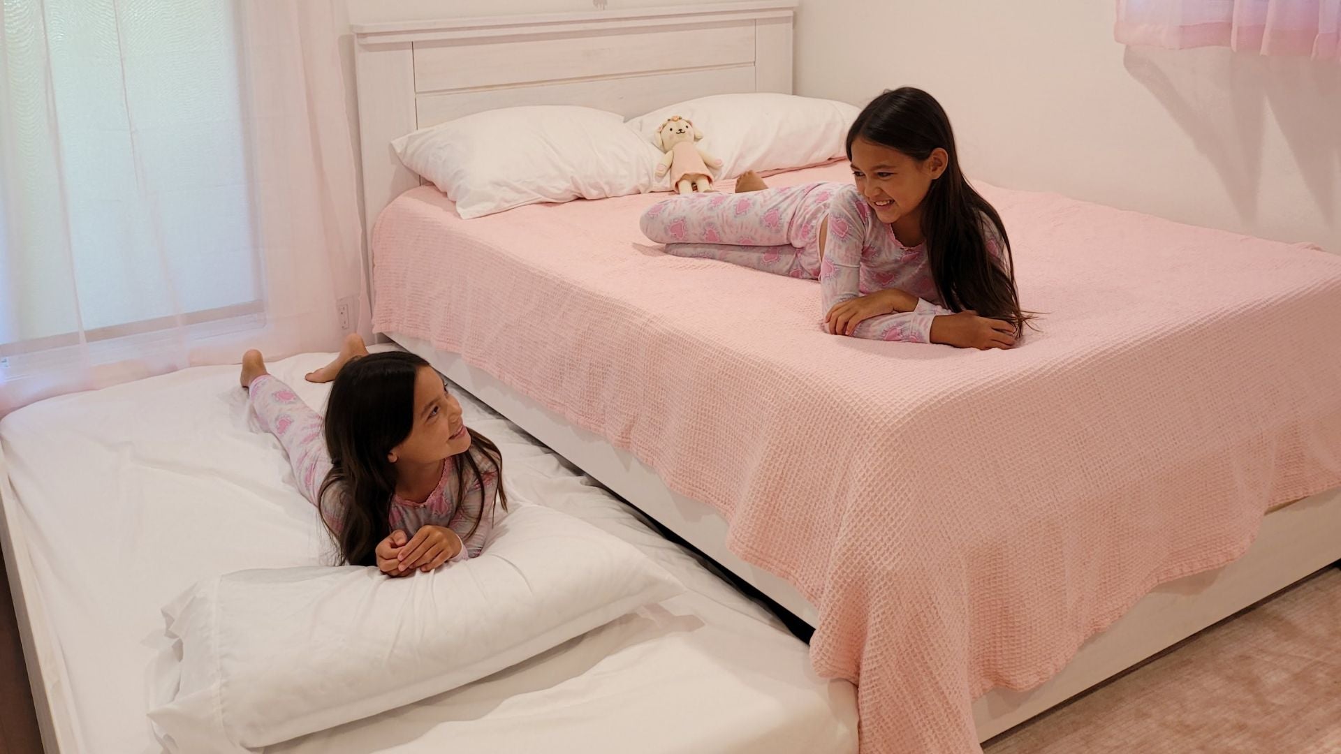 White full-size bed with trundle bed and panel headboard in pink girls' room