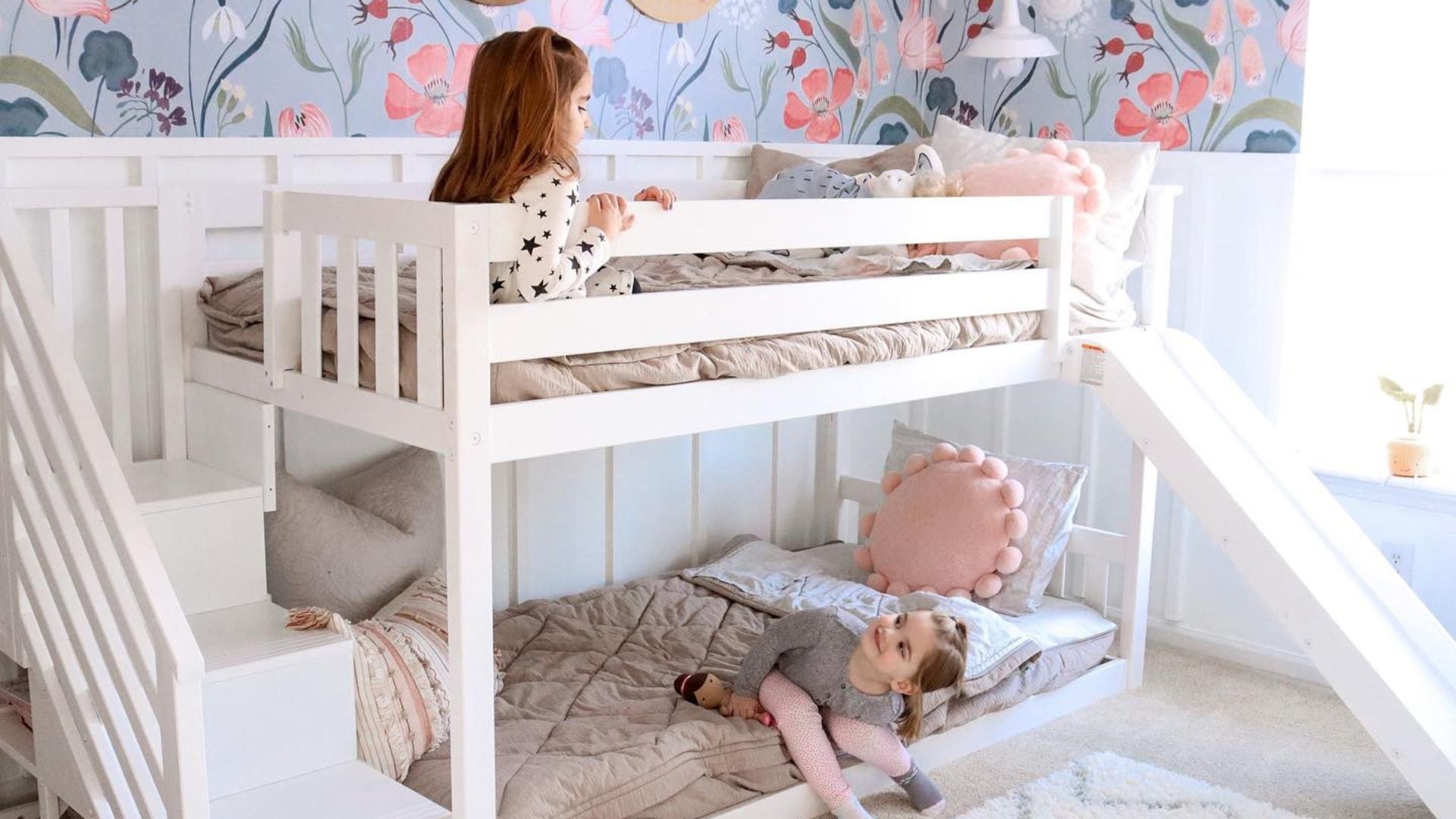 Sisters hanging out in twin low bunk bed with stairs and slide in white with floral wallpaper